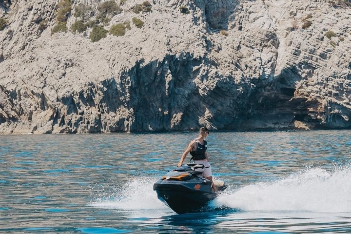 Person riding a jet ski on clear water near rocky cliffs.