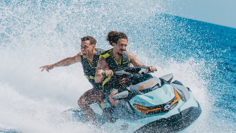 Two people riding a jet ski on the ocean, creating a large splash.
