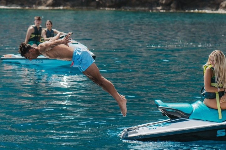 Man diving from jet ski into blue water, woman sitting on another jet ski.