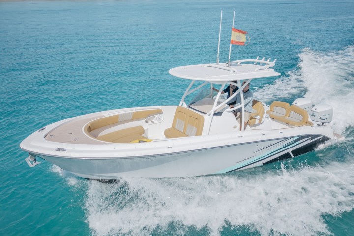 Motorboat with Spanish flag cruising on turquoise water near a mountainous coastline.