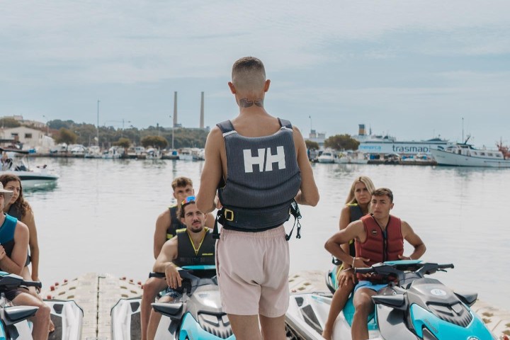 Instructor briefing group on jet skis at a marina.