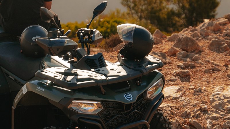 Person on an ATV parked on a rocky terrain with a scenic background.