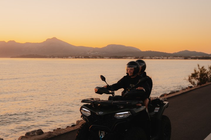 People on an ATV ride along a coastal road at sunset.