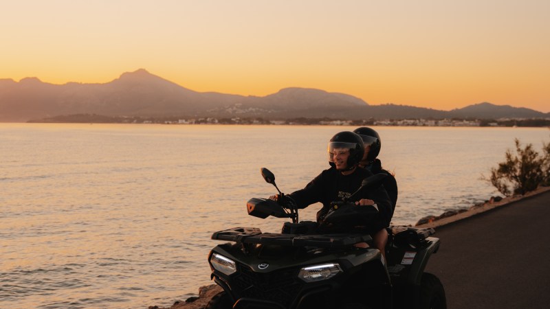 People on an ATV ride along a coastal road at sunset.