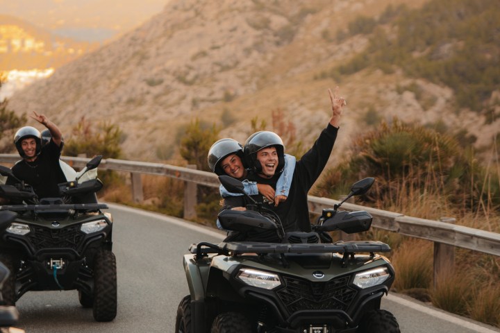 People riding ATVs on a scenic mountain road, smiling and waving.