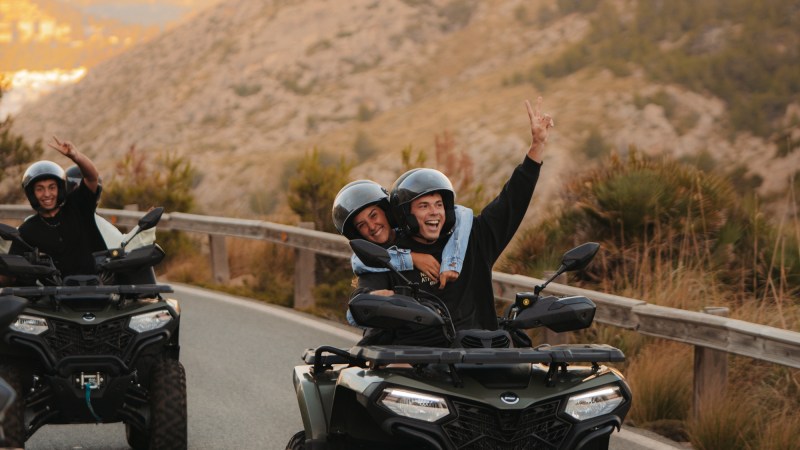 People riding ATVs on a scenic mountain road, smiling and waving.
