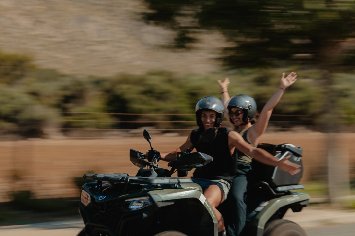 Two people riding a quad bike on a road with blurred background.