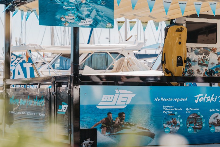 Jet ski rental booth with banners and photos, boats and marina in background.