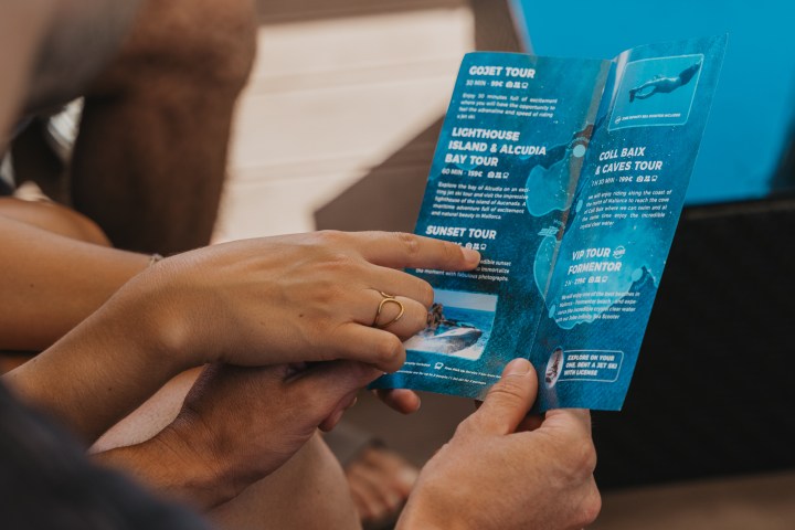 Two people reading a blue brochure with tourism information while sitting outside.