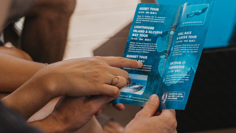 Two people reading a blue brochure with tourism information while sitting outside.
