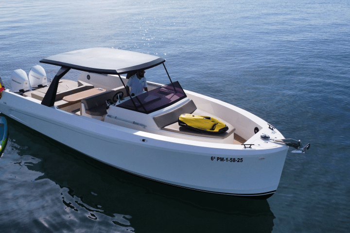 White motorboat with sunshade and paddleboard on calm water, person steering.