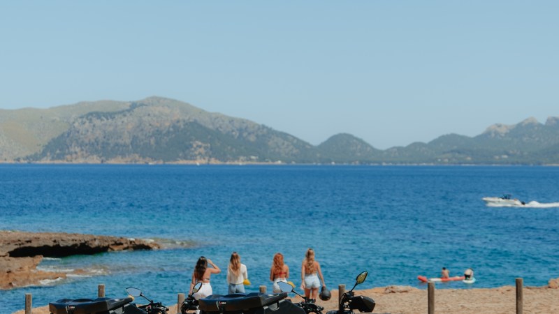 Two ATVs parked by a scenic beach with people and mountains in the background.