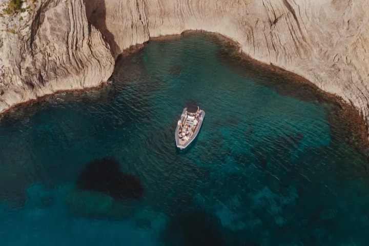 Aerial view of a boat in clear blue water near rocky cliffs.