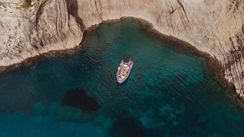 Aerial view of a boat in clear blue water near rocky cliffs.