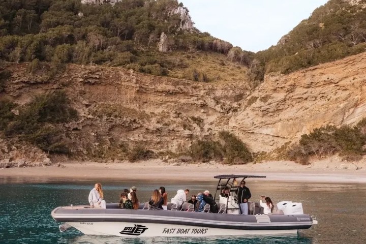 Tourists on a boat near a rocky, forested coastline.