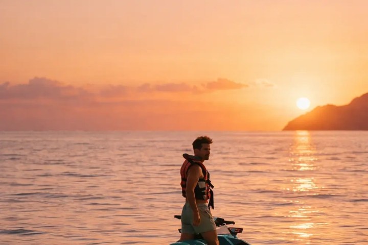 Person on a jet ski at sea during sunset, with a mountainous silhouette in the background.