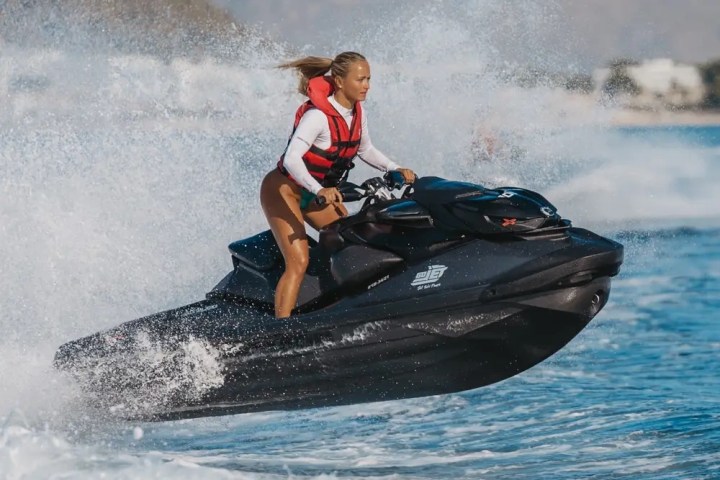 Person riding a jet ski over waves with mountains in the background.